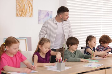 Man teaching kids to draw at painting lesson indoors