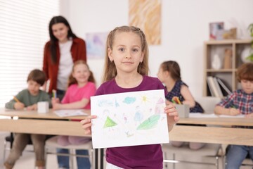 Fototapeta premium Cute girl showing her drawing during painting lesson indoors, selective focus