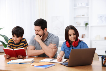 Father helping his kids with homework at wooden table indoors