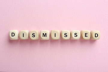 Word Dismissed made of wooden cubes on pink background, top view