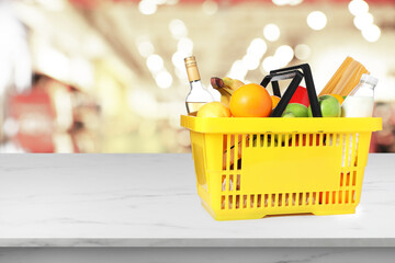 Yellow shopping basket full of groceries on marble table in supermarket. Space for text
