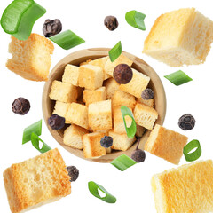 Delicious crispy croutons, green onion and peppercorns falling into bowl on white background, top view
