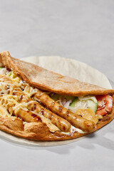 Gyros with grilled sausages on flatbread, creamy sauce, vibrant daylight, minimalistic composition