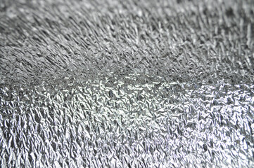 Shiny metallic crinkled surface with a diagonal texture. Reflective foil material creating an abstract industrial pattern.