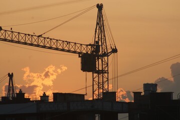 Sanset over city with silhouette of construction crane and building.