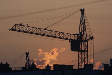 Obraz premium Sanset over city with silhouette of construction crane and building.