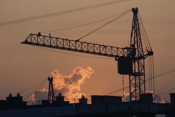 Obraz premium Sanset over city with silhouette of construction crane and building.