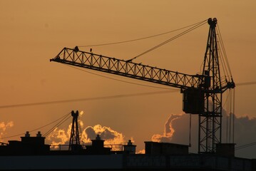 Obraz premium Sanset over city with silhouette of construction crane and building.