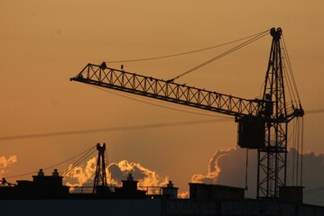 Obraz premium Sanset over city with silhouette of construction crane and building.