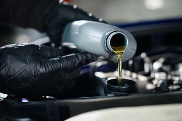 Worker pouring motor oil from bottle into car engine, closeup