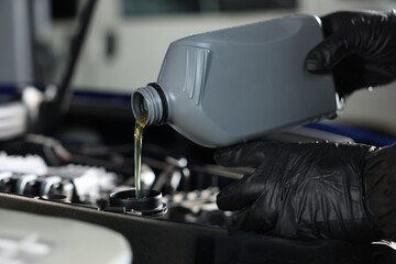 Worker pouring motor oil from canister into car engine, closeup