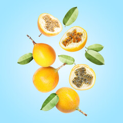 Delicious ripe passion fruits with green leaves falling on light blue background