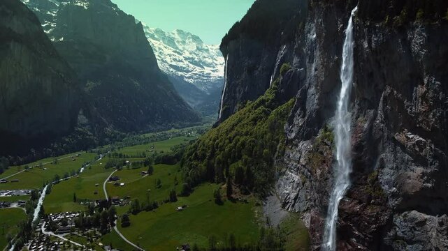 Aerial drone view of the stunning Staubbach Falls in Switzerland, cascading down the cliffside into the valley below, surrounded by lush greenery and rugged terrain.