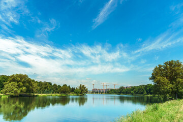 Sunny summer landscape on the lake. Reflection of the sky and clouds in the water. A valley of green trees on the shore of a lake. A concept for travel and camping.