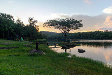 Tourists enjoy photographing the sunset at Pha Daen Forest Park, a tiny tree-covered island viewpoint with a beautiful bridge and warm golden hour light.