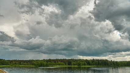 Grey rainy clouds over the lake. Dense forest along the lake shore during a storm.