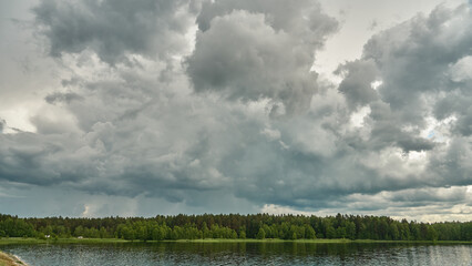 Grey rainy clouds over the lake. Dense forest along the lake shore during a storm.
