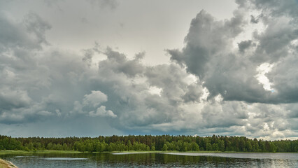 Grey rainy clouds over the lake. Dense forest along the lake shore during a storm.