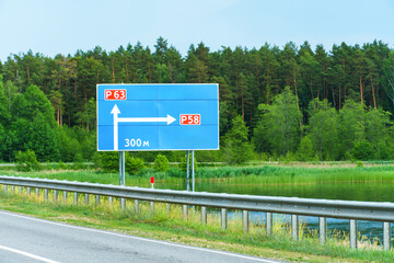 A road sign on an empty road along a forest and lake. A road sign indicating the direction of travel.
