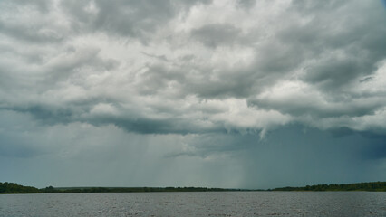 Grey rainy clouds over the lake. Dense forest along the lake shore during a storm.