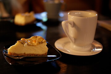 黒いプレートにのったチーズケーキと白いカップの温かなコーヒー

