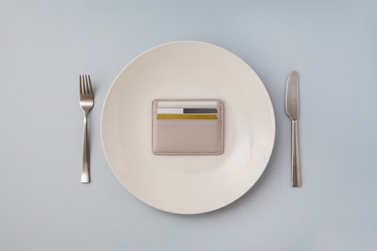 Card wallet lies on plate surrounded by fork and knife. Food expenses concept. Selective focus, copy space