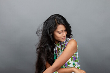 A confident young woman wearing a floral top poses gracefully in a studio setting, showcasing...