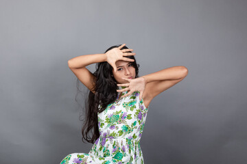 A confident young woman wearing a floral top poses gracefully in a studio setting, showcasing beauty, self-assurance, and style. Her long hair flows elegantly, adding movement, vibrancy to the picture