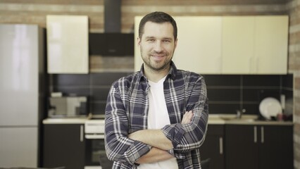 Happy young man posing at the kitchen with folded hands, looking at camera