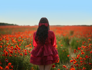 Sexy girl in short red dress posing on poppy field of flowers.