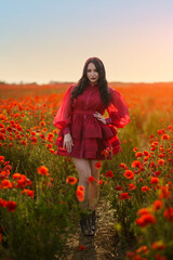 Sexy girl in short red dress posing on poppy field of flowers.
