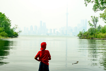 Wild fire smoke over a big city: a young person looks out from the Toronto Islands at the downtown...