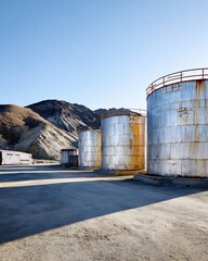Obraz premium industrial sulfuric acid storage tank in remote desert landscape, weathered metal containers against barren hills