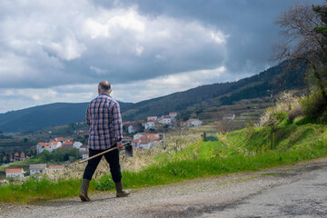 Farmer in a paid shirt, rubber boots and a hoe in his hand walking towards his field in Central Portugal. 