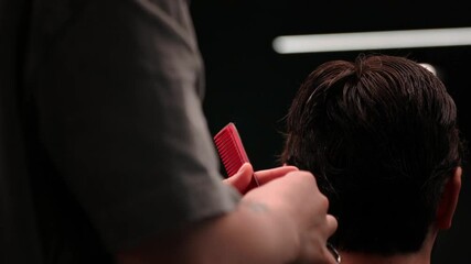 Close-up video of a barber expertly trimming a male client's hair with scissors. Hair clippings fall gently, showcasing precision grooming in a contemporary barbershop setting.
