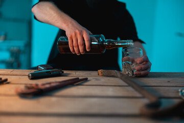 Close up of robber in black clothes pouring alcohol into a glass. Weapons on the table. Crime,...