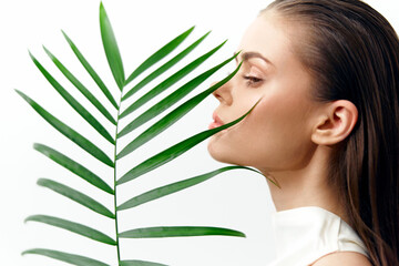 Fototapeta premium Portrait of a serene model with a palm leaf, showcasing elegance and tranquility in a minimalistic white background. KEYWORDS: model, palm, serenity, elegance, beauty, nature, minimalism