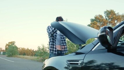 Guy standing near a broken car and opening the hood outdoors. Service car concept.