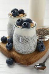 Delicious pudding with chia seeds, yogurt, blueberries and granola in glasses on white wooden table, closeup. Superfood