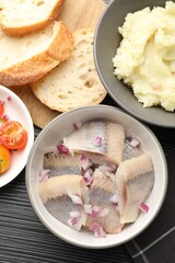 Delicious herring pieces with onions served on black wooden table, flat lay