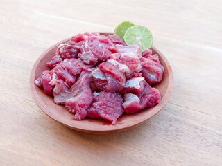 raw goat meat served with lime on a wooden plate on a wooden background.