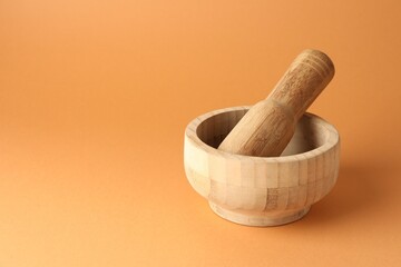 Wooden mortar and pestle on light brown background, closeup. Space for text