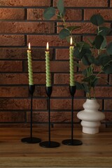 Candlesticks with burning candles on table near brick wall