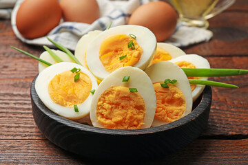 Halves of hard boiled eggs with green onions on wooden table, closeup