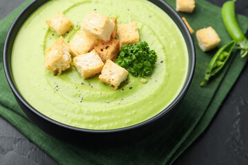 Tasty pea cream soup with croutons and broccoli served on black table, closeup