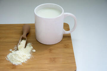 powdered milk with spoon  and  milk  in a white cup  on a wooden board.