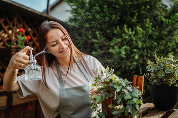Young woman taking care of plants with water can and mister	