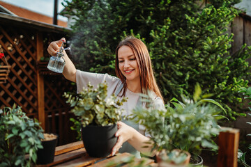 Young woman taking care of plants with water can and mister	