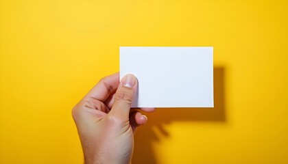 Obraz premium A hand holding a blank white card against a bright yellow background