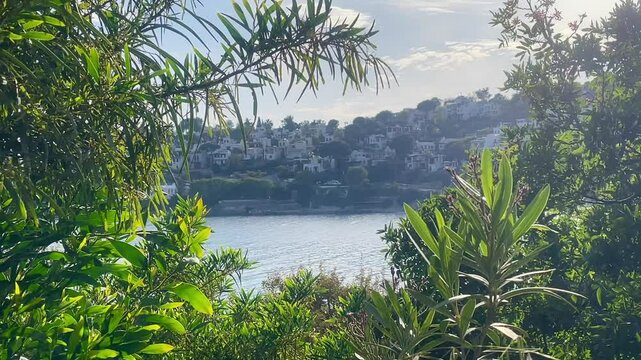 Framed by rich coastal foliage, the hillside homes near Bodrum, Turkey, rise above the glistening sea in the afternoon light, slow motion